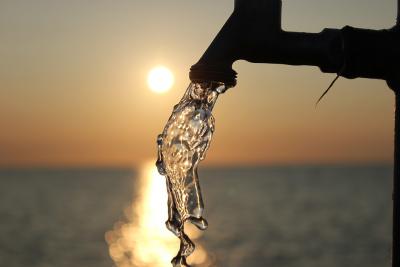 Water coming out of faucet in foreground, sunset at the beach in background